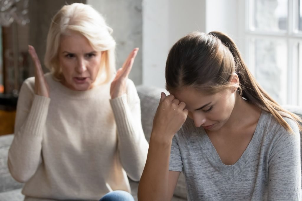 Mid aged mother sit on couch scold grown up daughter, angry mum tell complaints lecturing teen adult child feeling stressed, misunderstandings, generational gap, difficulties in relationships concept